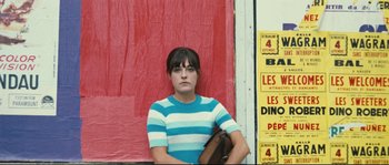 Movie still from “2 or 3 Things I Know About Her” (1967), directed by Jean-Luc Godard – A woman in a blue and white striped shirt holding a purse; Medium shot, Low angle