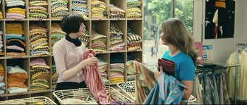 Movie still from “2 or 3 Things I Know About Her” (1967), directed by Jean-Luc Godard – Two women are talking in front of shelves of fabrics; Medium shot, Over the shoulder angle