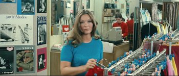 Movie still from “2 or 3 Things I Know About Her” (1967), directed by Jean-Luc Godard – A woman in a blue shirt holding a pair of scissors in her hand; Medium shot, Over the shoulder angle