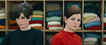 Movie still from “2 or 3 Things I Know About Her” (1967), directed by Jean-Luc Godard – Two people in front of a shelf of folded clothes; Medium shot, High angle