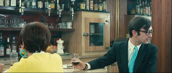Movie still from “2 or 3 Things I Know About Her” (1967), directed by Jean-Luc Godard – A man sitting at a table holding a glass of wine; Medium shot, Over the shoulder angle