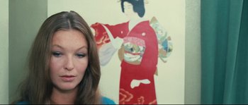 Movie still from “2 or 3 Things I Know About Her” (1967), directed by Jean-Luc Godard – A woman standing in front of a painting of a geisha; Close Up shot, Over the shoulder angle