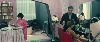 Movie still from “2 or 3 Things I Know About Her” (1967), directed by Jean-Luc Godard – A man standing next to a woman in front of a hair dryer; Medium shot, Over the shoulder angle