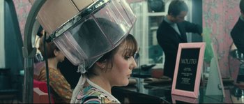 Movie still from “2 or 3 Things I Know About Her” (1967), directed by Jean-Luc Godard – A woman sitting in front of a mirror with a hair dryer on her head; Close Up shot, Over the shoulder angle