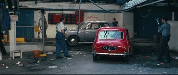 Movie still from “2 or 3 Things I Know About Her” (1967), directed by Jean-Luc Godard – Two men working in a car repair shop; Wide shot, High angle