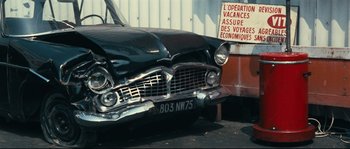 Movie still from “2 or 3 Things I Know About Her” (1967), directed by Jean-Luc Godard – An old car with a sign on the side of the road; Medium shot, Low angle