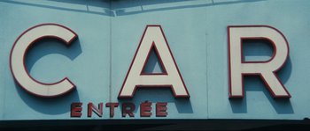 Movie still from “2 or 3 Things I Know About Her” (1967), directed by Jean-Luc Godard – A sign that is on the side of a building; Extreme Wide shot, Low angle