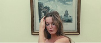 Movie still from “2 or 3 Things I Know About Her” (1967), directed by Jean-Luc Godard – A woman sitting in front of a painting of a ship; Close Up shot, Low angle
