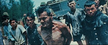 Movie still from “2 or 3 Things I Know About Her” (1967), directed by Jean-Luc Godard – A group of men standing next to each other on a dirt road; Medium shot, High angle