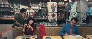 Movie still from “2 or 3 Things I Know About Her” (1967), directed by Jean-Luc Godard – A woman sitting at a booth in a restaurant; Medium shot, High angle
