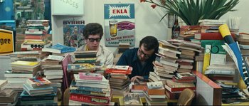 Movie still from “2 or 3 Things I Know About Her” (1967), directed by Jean-Luc Godard – Two men sitting in front of a pile of books; Medium shot, High angle