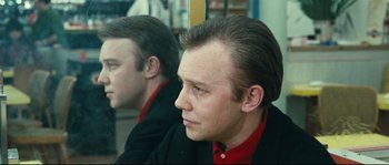 A man in a red and black shirt looking at his reflection in a mirror