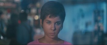 Movie still from “2 or 3 Things I Know About Her” (1967), directed by Jean-Luc Godard – A woman with short black hair wearing a pink shirt; Close Up shot, High angle