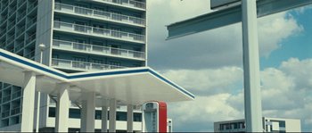 Movie still from “2 or 3 Things I Know About Her” (1967), directed by Jean-Luc Godard – A gas station with a building in the background; Extreme Wide shot, Low angle