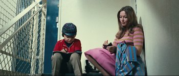 Movie still from “2 or 3 Things I Know About Her” (1967), directed by Jean-Luc Godard – A woman sitting next to a young boy writing on a piece of paper; Medium shot, High angle