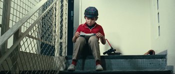 Movie still from “2 or 3 Things I Know About Her” (1967), directed by Jean-Luc Godard – A boy sitting on the steps reading a book; Medium shot, High angle