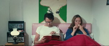 Movie still from “2 or 3 Things I Know About Her” (1967), directed by Jean-Luc Godard – A man and a woman sitting on a bed reading a book; Medium shot, High angle