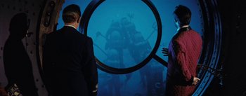 Movie still from “20,000 Leagues Under the Sea” (1954), directed by Richard Fleischer – A man looking at a submarine through a magnifying glass; Wide shot, Over the shoulder angle