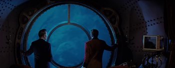 Movie still from “20,000 Leagues Under the Sea” (1954), directed by Richard Fleischer – A man standing in front of a large circular window; Wide shot, Over the shoulder angle