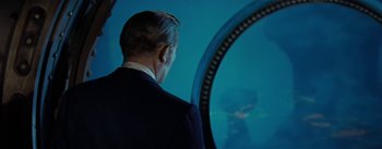 Movie still from “20,000 Leagues Under the Sea” (1954), directed by Richard Fleischer – A man in a suit looking out a window; Medium shot, Over the shoulder angle