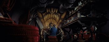 Movie still from “20,000 Leagues Under the Sea” (1954), directed by Richard Fleischer – A man sitting in front of an organ in a room; Wide shot, Overhead angle
