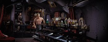 Movie still from “20,000 Leagues Under the Sea” (1954), directed by Richard Fleischer – A man standing in front of a table with bottles on top of it; Wide shot, High angle