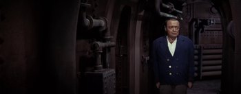 Movie still from “20,000 Leagues Under the Sea” (1954), directed by Richard Fleischer – A man in a suit standing next to pipes in a room; Medium shot, High angle