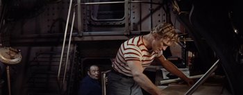 Movie still from “20,000 Leagues Under the Sea” (1954), directed by Richard Fleischer – A man standing next to another man in a room; Medium shot, High angle