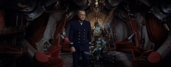 Movie still from “20,000 Leagues Under the Sea” (1954), directed by Richard Fleischer – A man in a suit standing in front of a fireplace; Wide shot, High angle