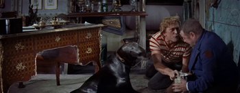 Movie still from “20,000 Leagues Under the Sea” (1954), directed by Richard Fleischer – A man sitting on the ground next to a black dog; Medium shot, High angle