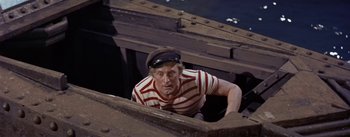 Movie still from “20,000 Leagues Under the Sea” (1954), directed by Richard Fleischer – A man wearing a hat and a striped t - shirt climbing up the side of a boat; Medium shot, Overhead angle