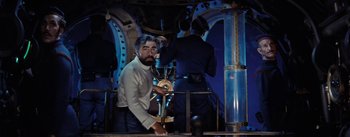 Movie still from “20,000 Leagues Under the Sea” (1954), directed by Richard Fleischer – A man holding a steering wheel in front of two men in blue suits; Medium shot, Low angle