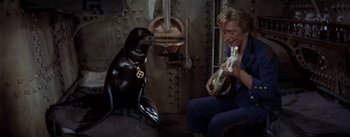 Movie still from “20,000 Leagues Under the Sea” (1954), directed by Richard Fleischer – A seal sitting next to a man holding a guitar; Medium shot, High angle