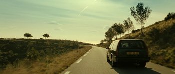 Movie still from “22 Bullets” (2010), directed by Richard Berry – A car driving down a road near some trees; Wide shot, Low angle