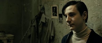 Movie still from “22 Bullets” (2010), directed by Richard Berry – A man standing in front of a wall with pictures on the wall; Close Up shot, Low angle