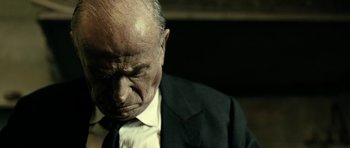 Movie still from “22 Bullets” (2010), directed by Richard Berry – An older man in a suit and tie looking down; Close Up shot, Low angle