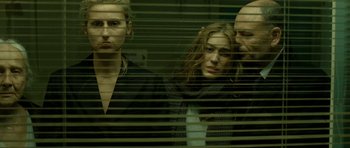 Movie still from “22 Bullets” (2010), directed by Richard Berry – A group of people standing in a room behind blinds; Medium shot, Over the shoulder angle
