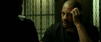 Movie still from “22 Bullets” (2010), directed by Richard Berry – A man with a shaved head sitting in front of a fence; Close Up shot, Over the shoulder angle