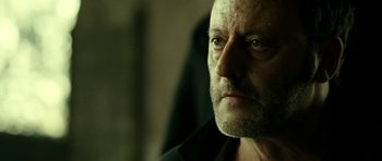 Movie still from “22 Bullets” (2010), directed by Richard Berry – An old man with a beard and a black shirt is looking into the distance; Close Up shot, Over the shoulder angle