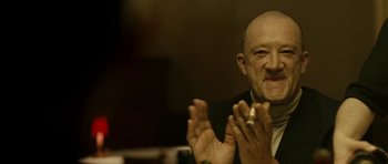 Movie still from “22 Bullets” (2010), directed by Richard Berry – An older man clapping his hands while wearing a suit; Close Up shot, Low angle