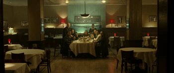 Movie still from “22 Bullets” (2010), directed by Richard Berry – A group of people sitting around a table with a plate of food; Wide shot, High angle