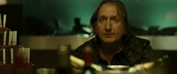 Movie still from “22 Bullets” (2010), directed by Richard Berry – A man sitting in front of a table with food on top of it; Close Up shot, Over the shoulder angle