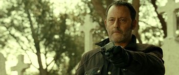 Movie still from “22 Bullets” (2010), directed by Richard Berry – A person holding a gun near a cross; Close Up shot, Low angle