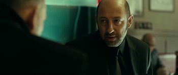 Movie still from “22 Bullets” (2010), directed by Richard Berry – A person wearing a suit and tie; Close Up shot, Over the shoulder angle