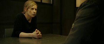 Movie still from “22 Bullets” (2010), directed by Richard Berry – A woman sitting at a table in a dark room; Medium shot, Over the shoulder angle