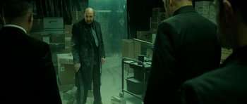 Movie still from “22 Bullets” (2010), directed by Richard Berry – A man in a suit and tie standing next to another man in a suit and tie; Medium shot, Over the shoulder angle