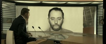 Movie still from “22 Bullets” (2010), directed by Richard Berry – A man with a goatee is sitting in front of a screen; Close Up shot, Over the shoulder angle