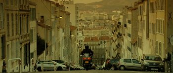 Movie still from “22 Bullets” (2010), directed by Richard Berry – A person riding a motorcycle down a street; Extreme Wide shot, Low angle