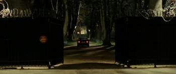 Movie still from “22 Bullets” (2010), directed by Richard Berry – A car driving down a street at night through a gate; Extreme Wide shot, Low angle