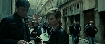 Movie still from “22 Bullets” (2010), directed by Richard Berry – A woman is walking down the street while holding a book; Medium shot, Over the shoulder angle
